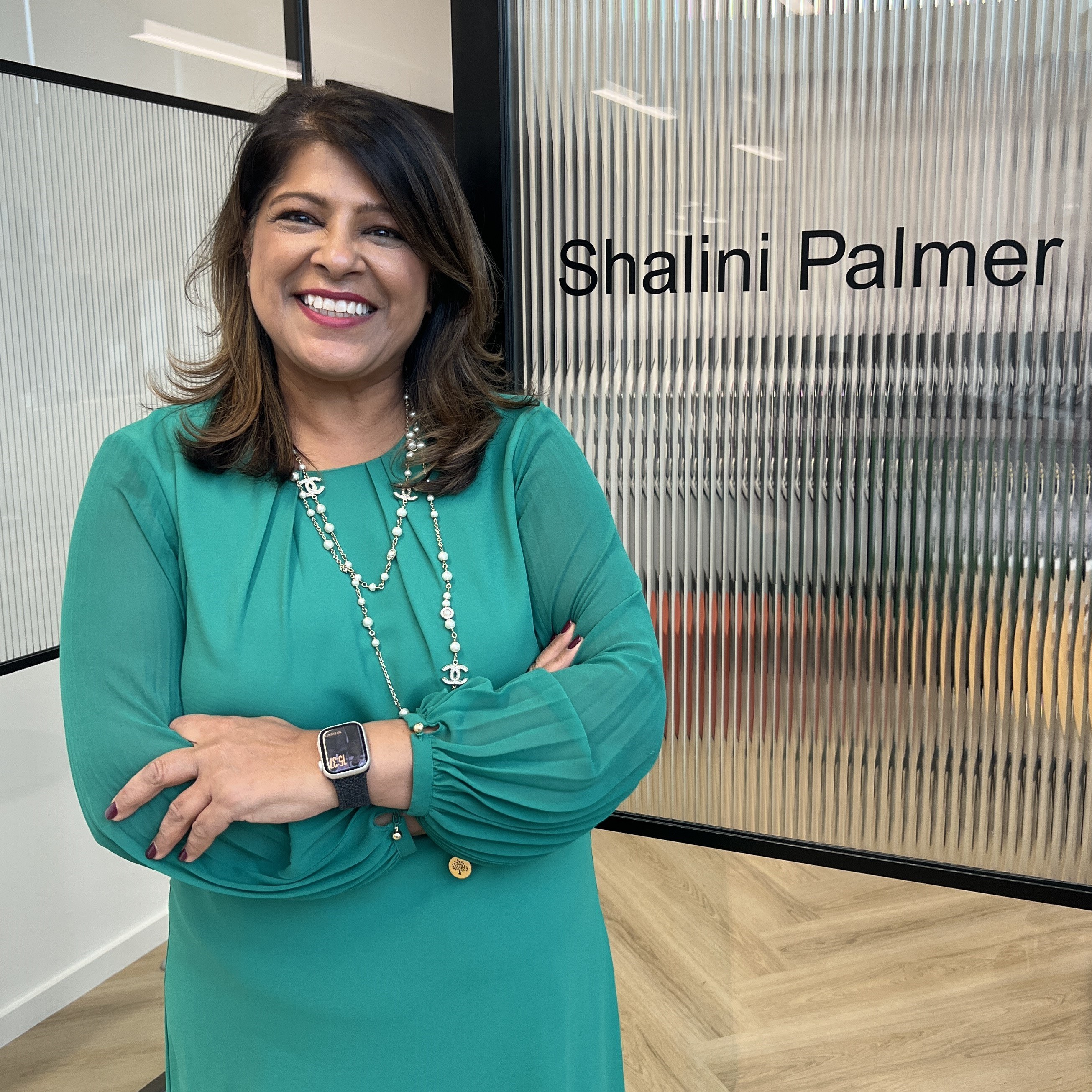 A photo of Shalini Palmer from Analog Devices - a woman of South Asian heritage in her 50s, with mid length dark hair, wearing a turquoise dress and gold necklaces.