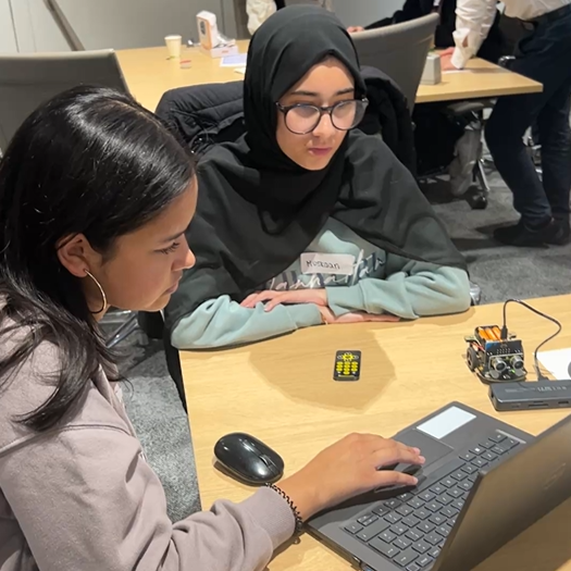 Two girls sit at a laptop, programming a Micro:bit robot at the Next Tech Girls Robotics Insight Day with Analog Devices.
