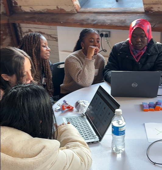 A group of young women sat round a table sharing laptops during a generative AI workshop at the Next Tech Girls and Mastek Insight Day in Manchester.