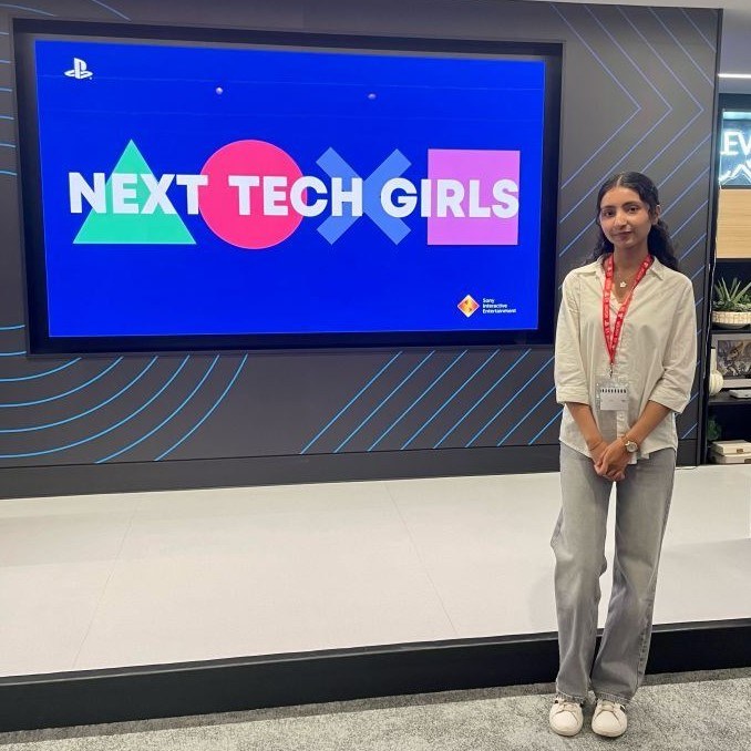 A photo of a young woman standing next to a screen with Next Tech Girls and the PlayStation logos on it