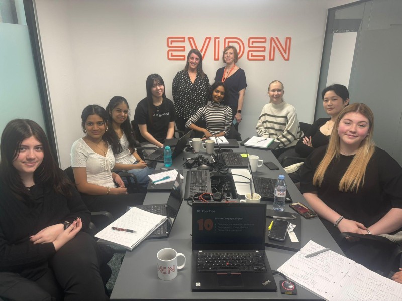 Students and Eviden staff sit around a desk posing for a photo