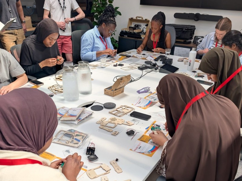A group of young women sit around a table making RF radios