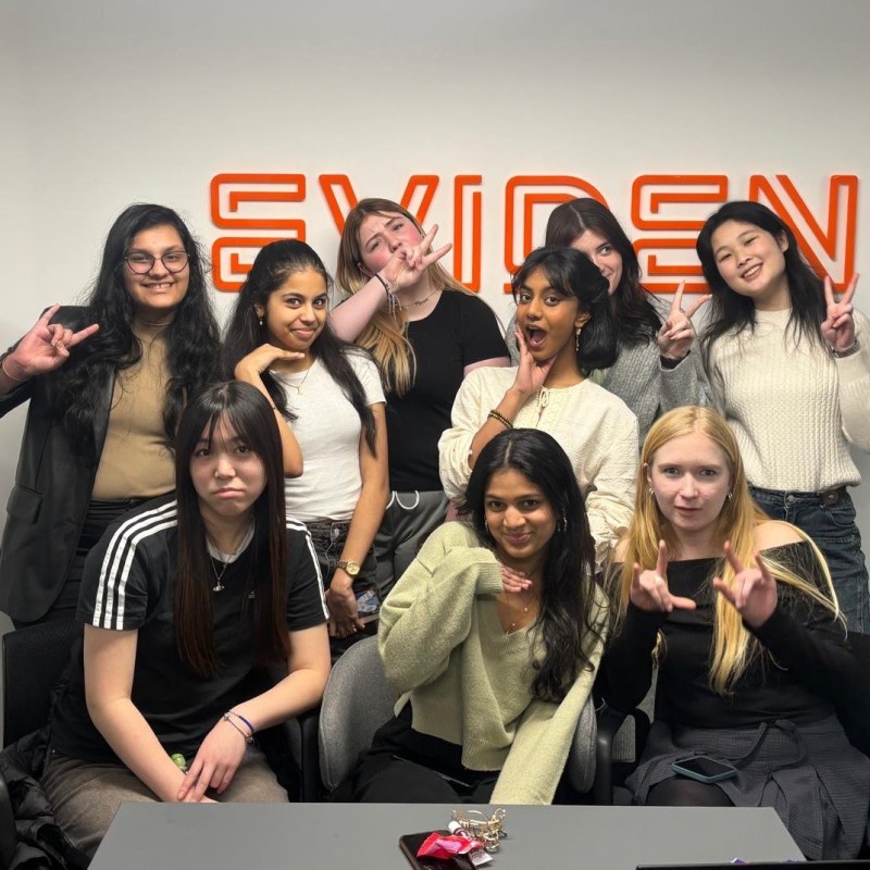 A group of young women pose in front of a large orange 'Eviden' sign during their work experience with Eviden and Atos.