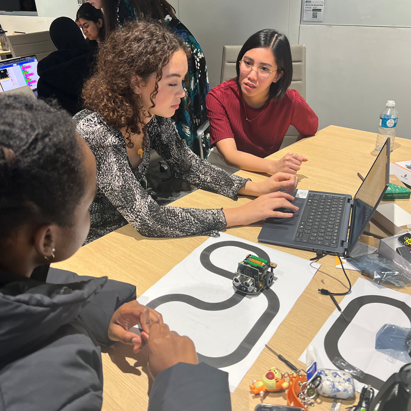 A woman from Analog Devices helps two students to programme a Micro:bit robot at the Next Tech Girls Robotics Insight Day.