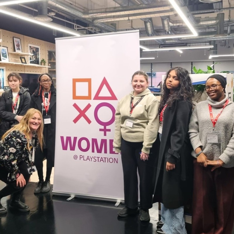A group of young women pose next to a Women at PlayStation sign