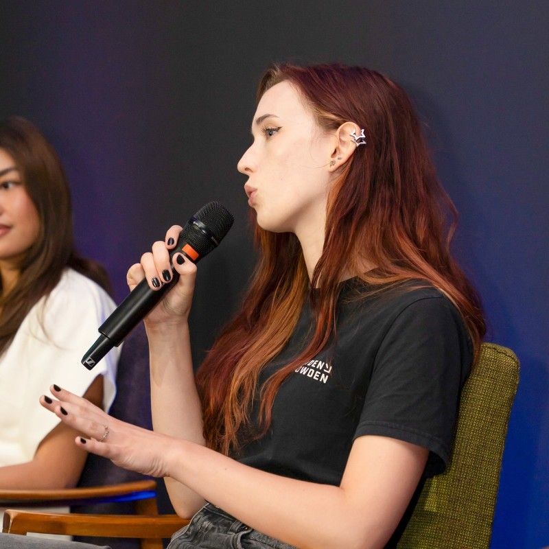 A young white woman speaking into a microphone on a panel at Next Tech Fest