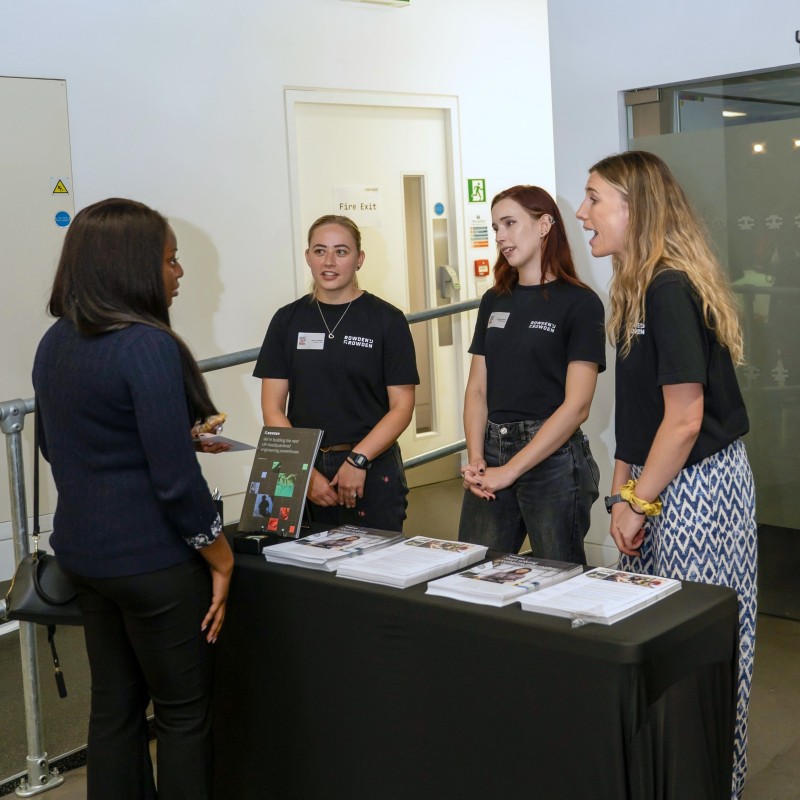 Three young women in Rowden t-shirts speaking to a young woman at an exhibition stand at Next Tech Fest